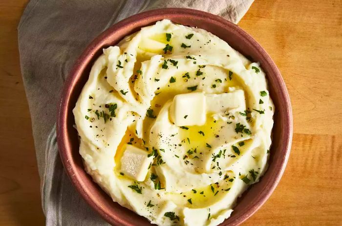 A top-down shot of creamy mashed potatoes, topped with melting butter and a sprinkle of fresh parsley