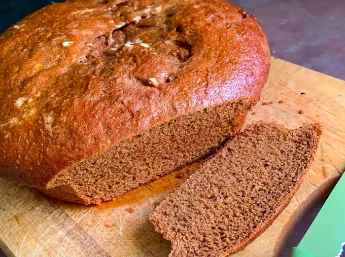 Close-up of a slice of pumpernickel bread resting on a wooden cutting board.