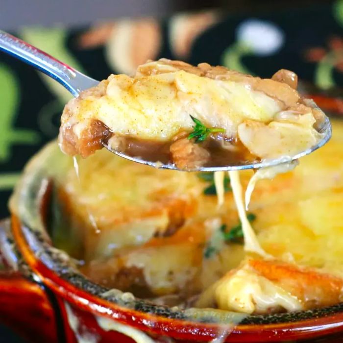 a close-up shot of a spoon scooping a cheesy bite from a bowl of French onion soup