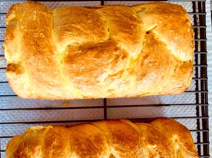 A close-up view of two loaves of golden-brown brioche cooling on a rack.