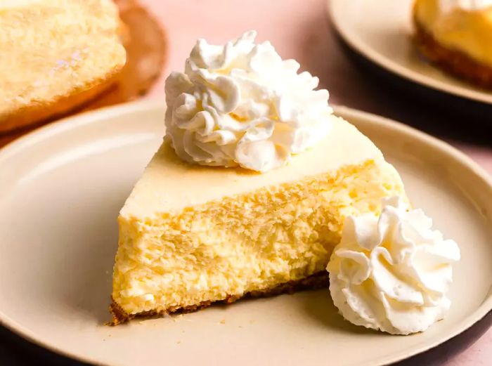 A close-up shot of a slice of eggnog cheesecake, elegantly plated and topped with a generous dollop of freshly whipped cream.