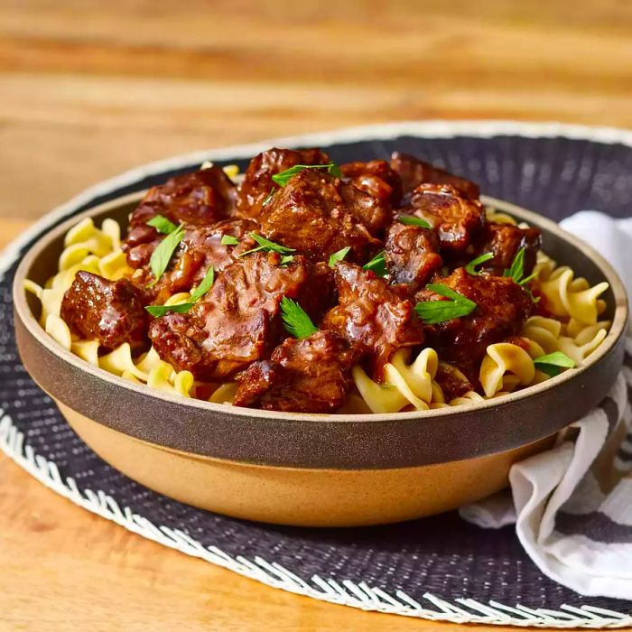 Mid-shot of a bowl of beef tips served on a bed of egg noodles.