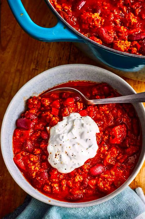 A top-down shot of a bowl filled with delicious chili, topped with a dollop of sour cream.