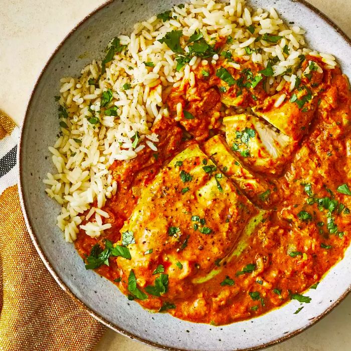 An overhead close-up of a bowl of Indian chicken curry served with rice and garnished with fresh cilantro.