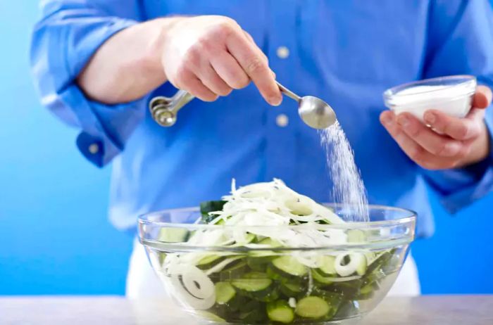 person adding canning salt to a bowl of pickles and onions