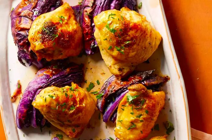 A close-up shot of crispy, golden-brown baked chicken thighs served alongside roasted cabbage.