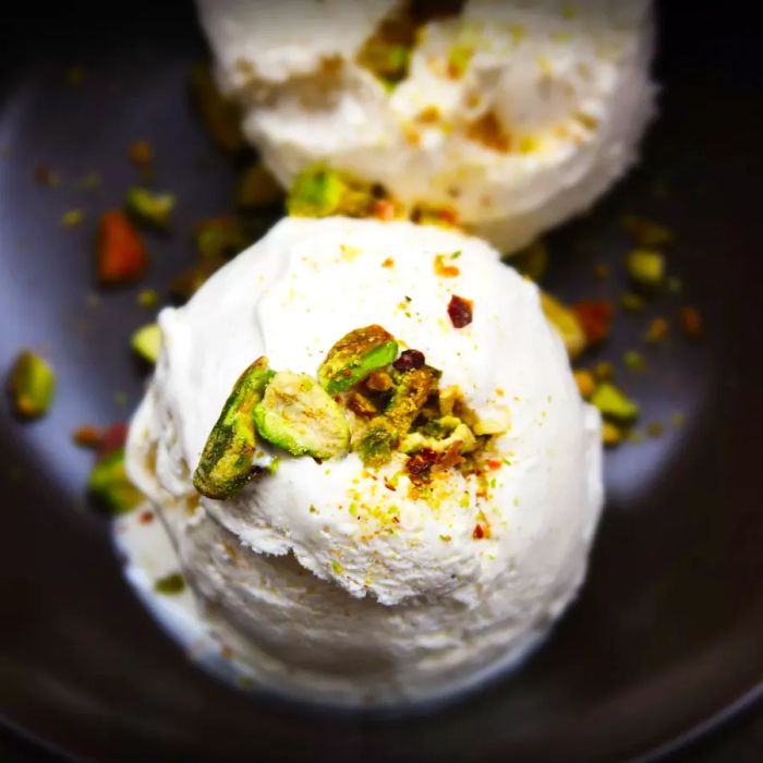 A close-up shot of two scoops of Kulfi ice cream topped with cardamom, served in a black bowl