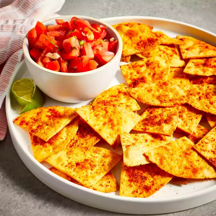 A close-up shot of a platter filled with golden-brown baked tortilla chips, accompanied by a side of fresh salsa.