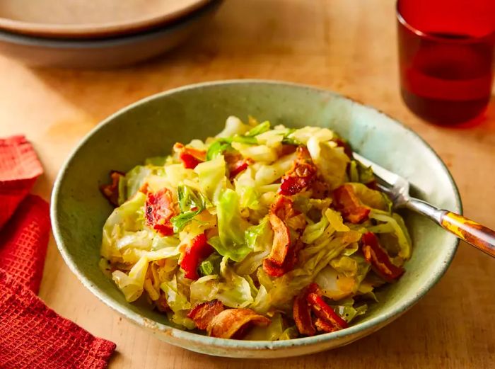 A single serving of fried cabbage with bacon and onions, served in a light green bowl.