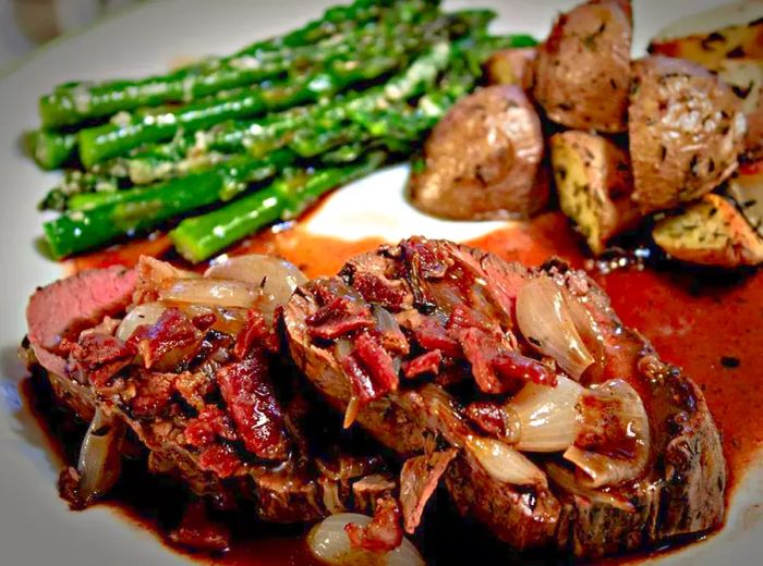 Close-up shot of Beef Tenderloin with Roasted Shallots, served alongside asparagus and potatoes on a white plate