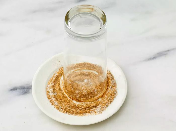 An overhead shot of a highball glass being rimmed with a mixture of salt and spices.