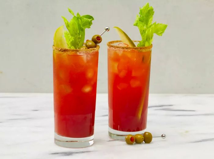 A close-up view of two highball glasses filled with Canadian Caesars, adorned with celery sticks, pickle spears, and olives