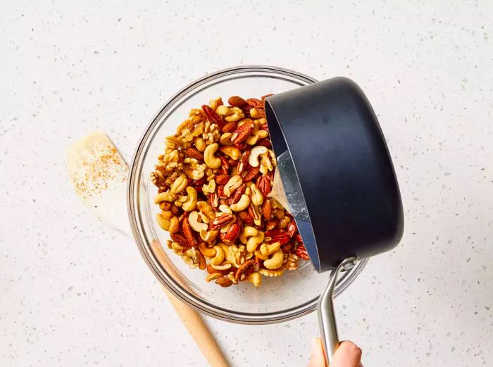 A pot of buttery syrup being drizzled over a bowl of spiced mixed nuts