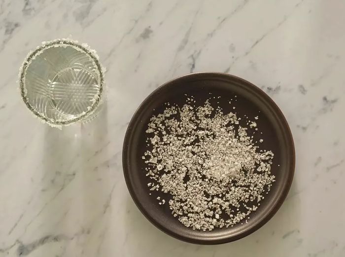 Overhead view of a plate of salt next to a glass with a salted rim.