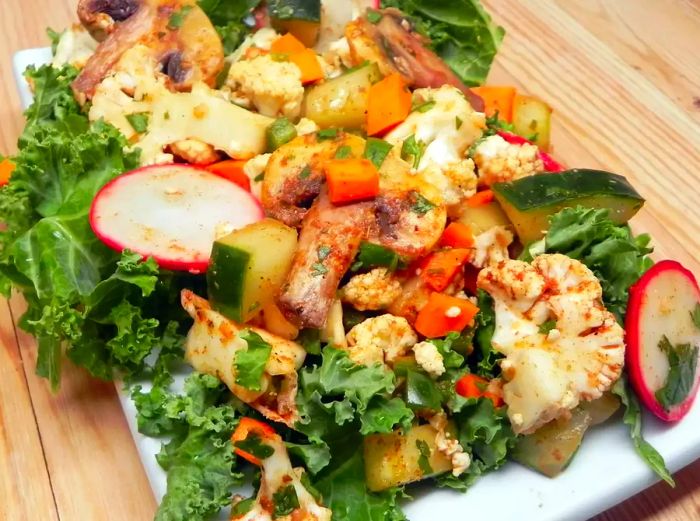 a vibrant kale salad with cucumber, cauliflower, mushrooms, carrot, and radishes arranged on a long white platter