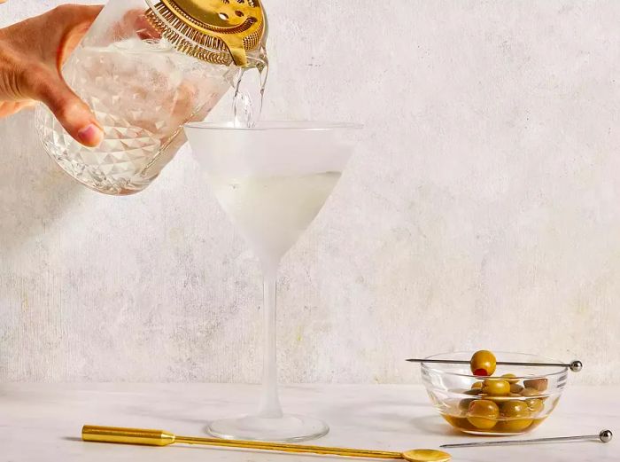 A low-angle shot captures a martini being poured into a glass from a strainer