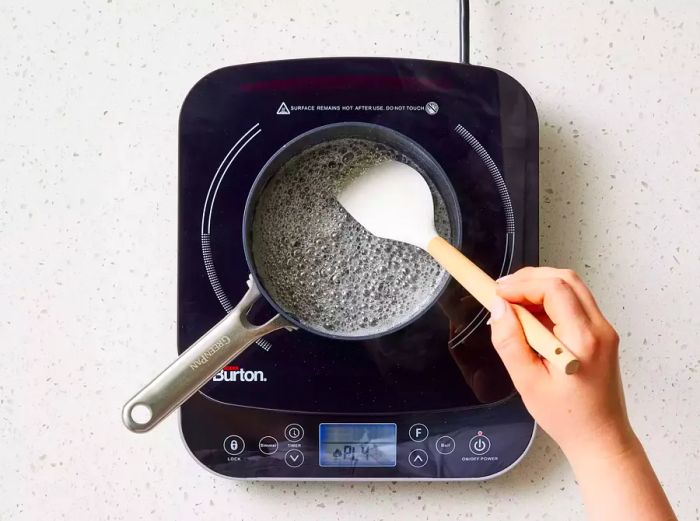 A pan of simmering sugar, butter, and water, being stirred with a rubber spatula