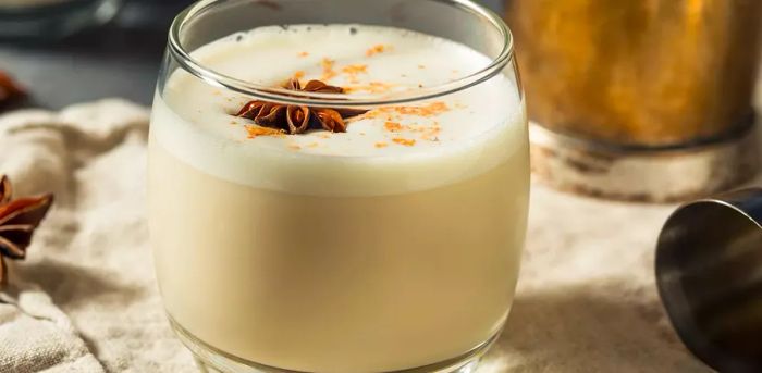 A glass of milk punch garnished with a dusting of spice and a star anise on top.