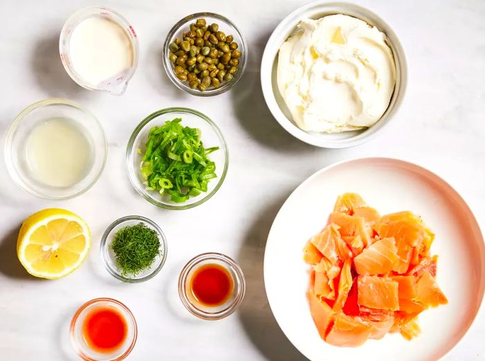 Bird's-eye view of the ingredients for the salmon spread arranged in various bowls and dishes.