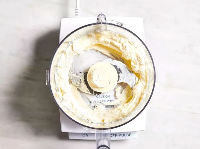 Bird's-eye view of cream cheese being processed in a food processor.