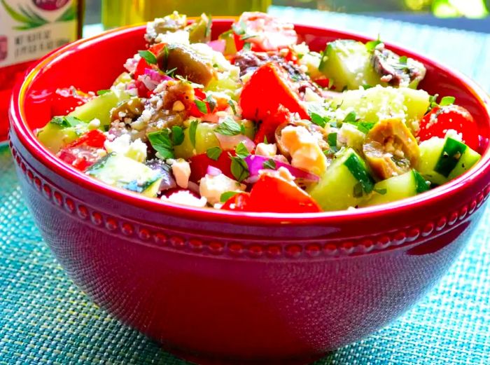 close-up of a red bowl brimming with a colorful salad featuring tomatoes, cucumber, and feta cheese