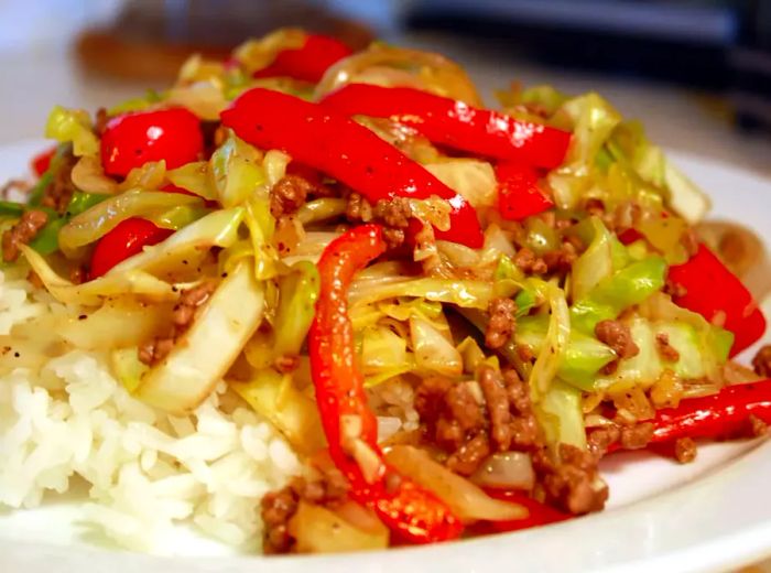 Slices of red bell pepper, shredded green cabbage, and ground beef served on a bed of white rice.