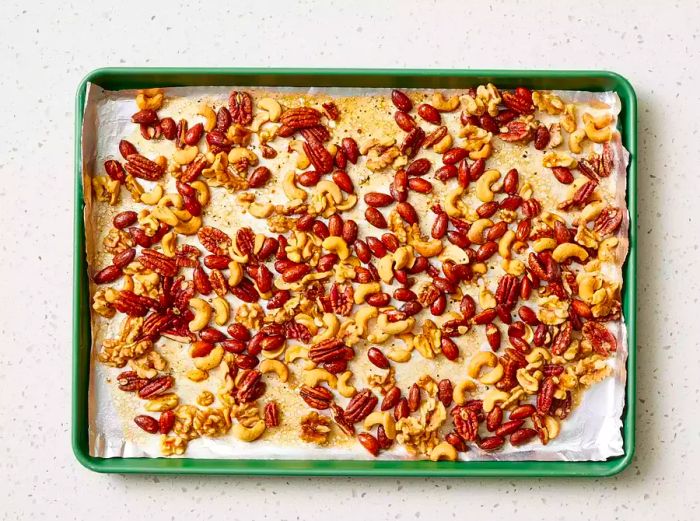 A baking sheet lined with foil, filled with a sweet, salty, and spicy mix of nuts