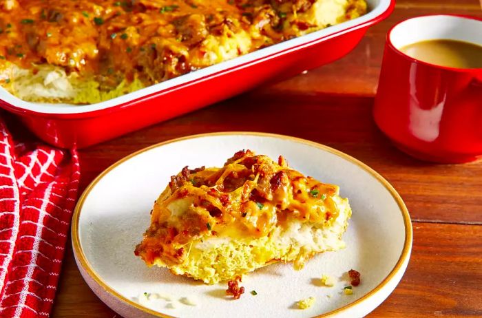 A plated portion of biscuit and gravy casserole sits before the red baking dish.