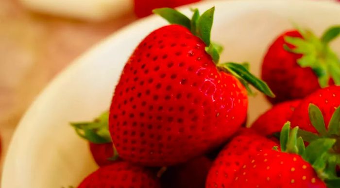 A close-up shot of a fresh strawberry in a white bowl.