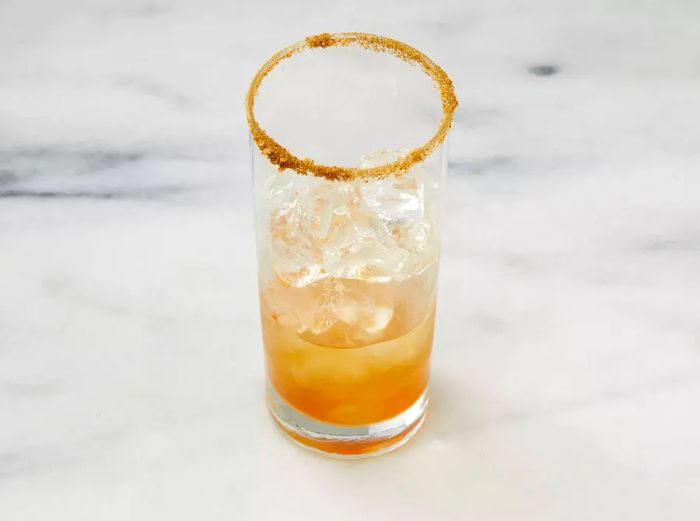 An overhead view of vodka and Worcestershire sauce being poured over ice in a highball glass with a spiced rim.