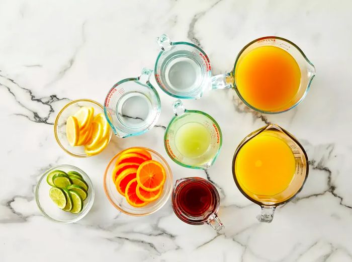 Aerial view of the rum punch ingredients arranged in bowls and measuring cups.