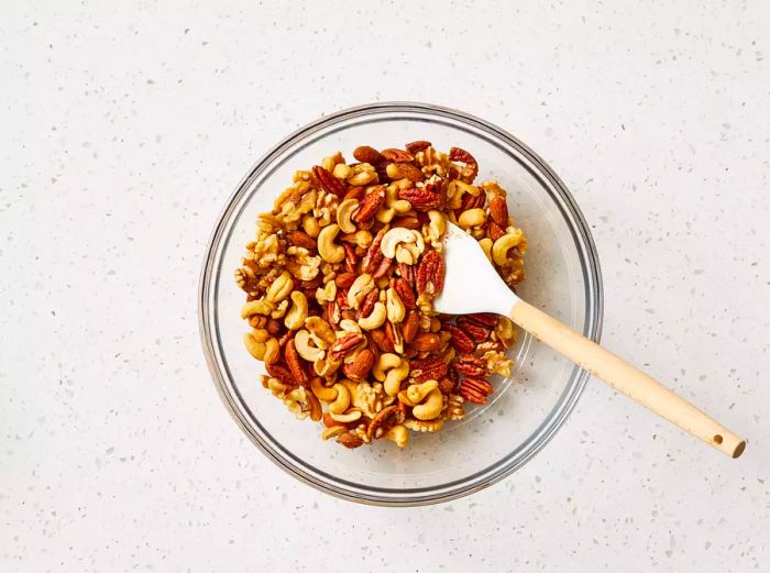 A large bowl of mixed nuts being stirred with a rubber spatula, coated in spices