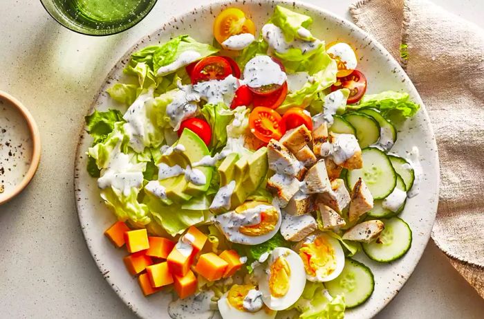 overhead shot of a chef's salad topped with grilled chicken and drizzled with black pepper ranch dressing