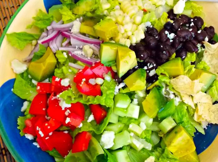 overhead shot of a romaine lettuce salad with black beans, corn, avocado, red onion, and tomato