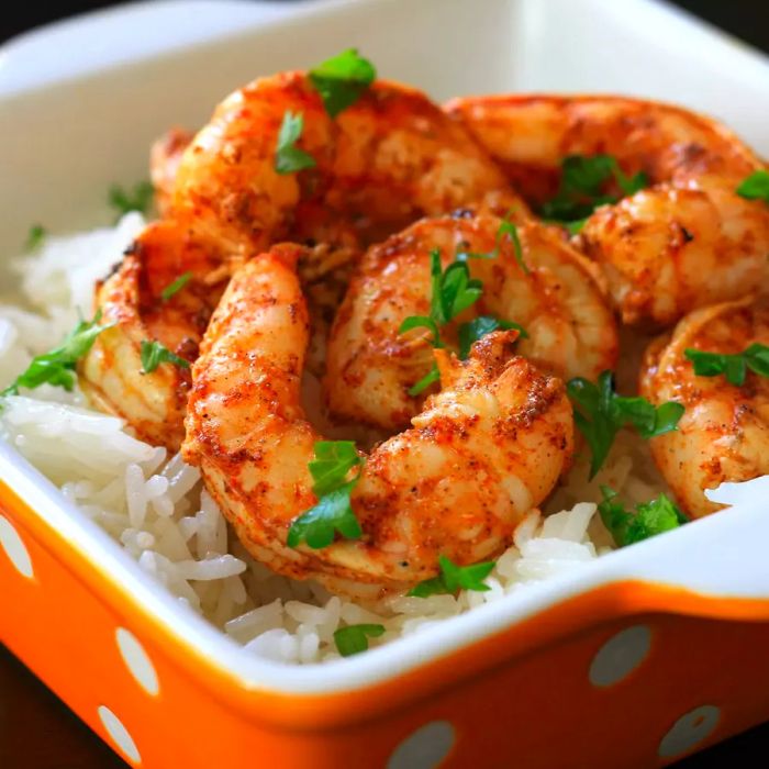 Grilled shrimp with parsley served over white rice in an orange bowl