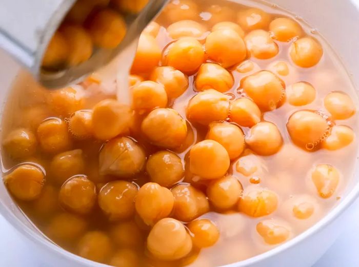 A close-up of chickpeas being poured from a can into a white bowl.