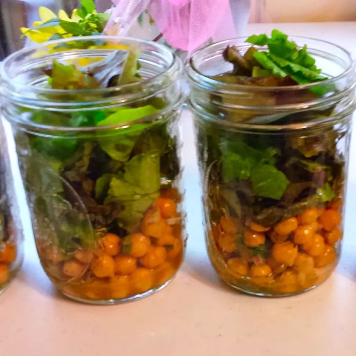 Two glass jars filled with chickpeas and leafy greens