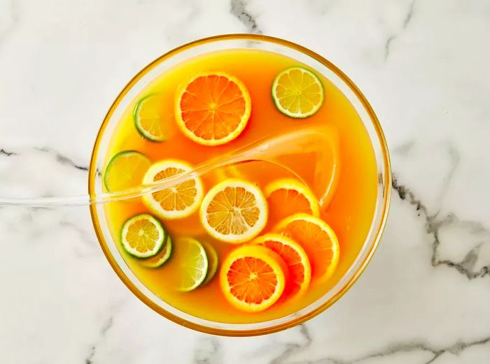 Aerial shot of orange and lime slices floating in rum punch inside a glass bowl.