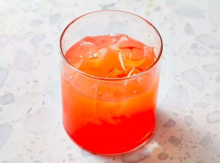 A high-angle shot of a rocks glass filled with ice, grenadine, and juice for the cocktail