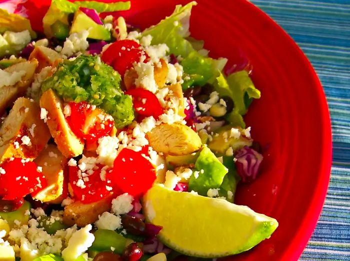 close-up of a salad in a red bowl, topped with a lime wedge