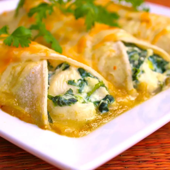 A close-up of spinach enchiladas garnished with fresh herbs on a white platter.