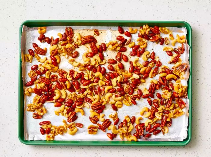 A baking sheet lined with foil, filled with mixed nuts coated in buttery syrup