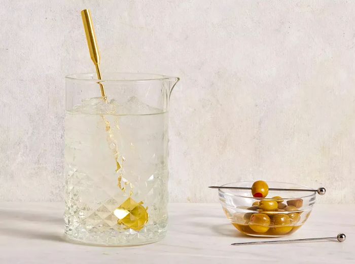 A front-facing view of a mixing glass and stirring spoon, filled with the ingredients for a martini