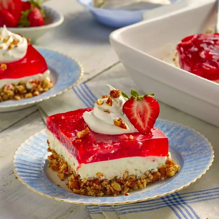 A square slice of Judy's Strawberry Pretzel Salad topped with whipped cream and garnished with a fresh strawberry.