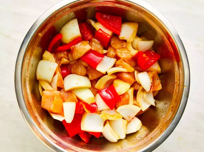 A bowl of chopped chicken, onions, bell peppers, and garlic soaking in the marinade.