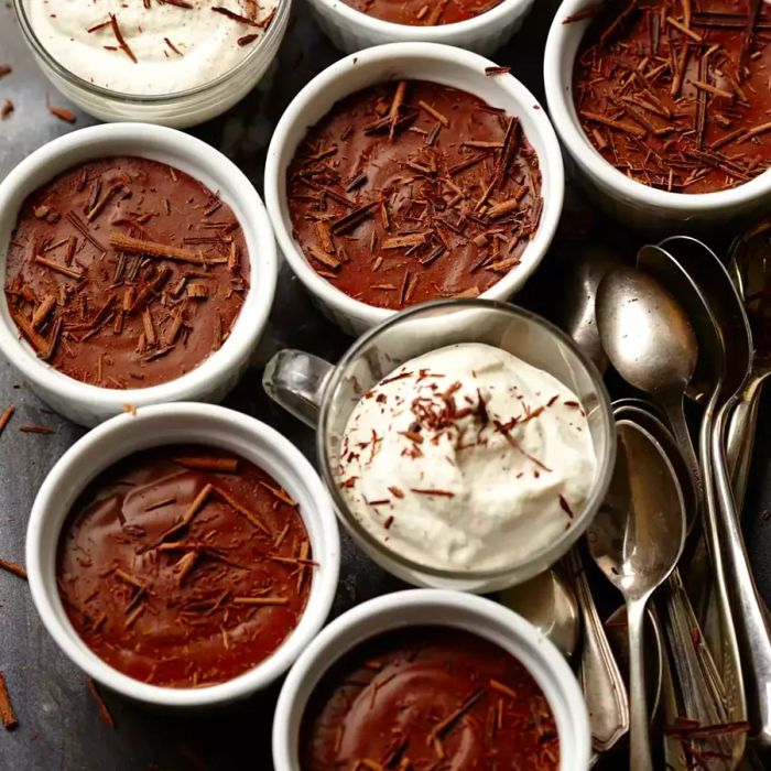 A top-down view of rich chocolate pots de creme, garnished with fluffy whipped cream and delicate chocolate shavings.