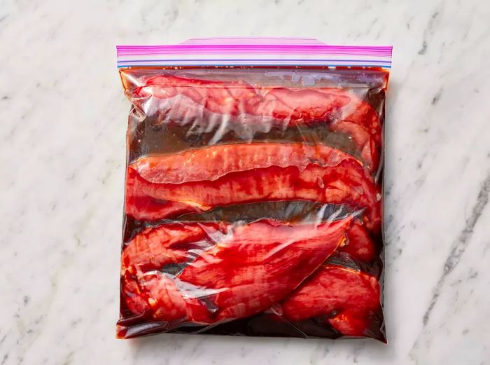 Pork slices placed in a plastic bag with the marinade, ready to be sealed and marinated.