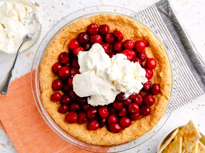 A top-down view of a puffed crust in a glass pie dish, beautifully adorned with fresh cherries and a scoop of vanilla ice cream.