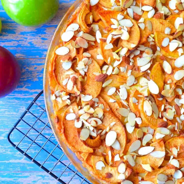 Close-up of an apple Bavarian torte with almond garnish resting on a cooling rack, surrounded by fresh apples.