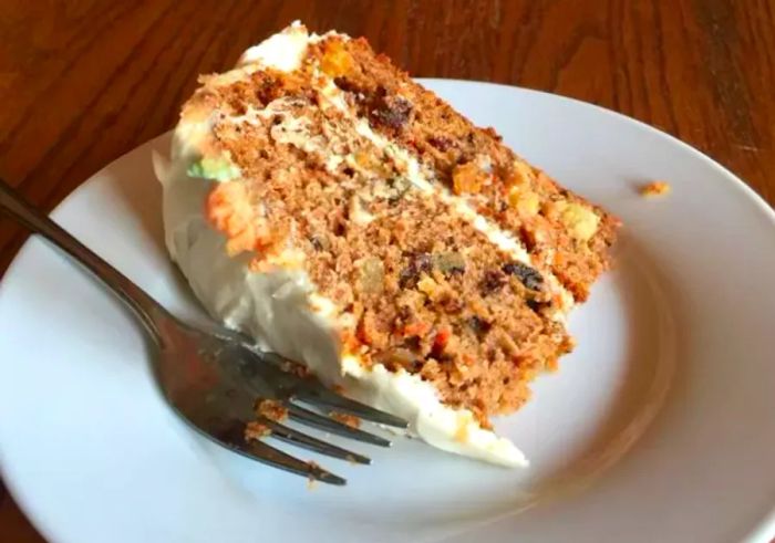 A slice of two-layer carrot cake with cream cheese frosting on a white plate